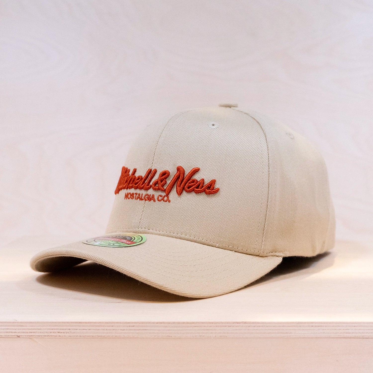 Beige cap with red logo on a light wooden surface