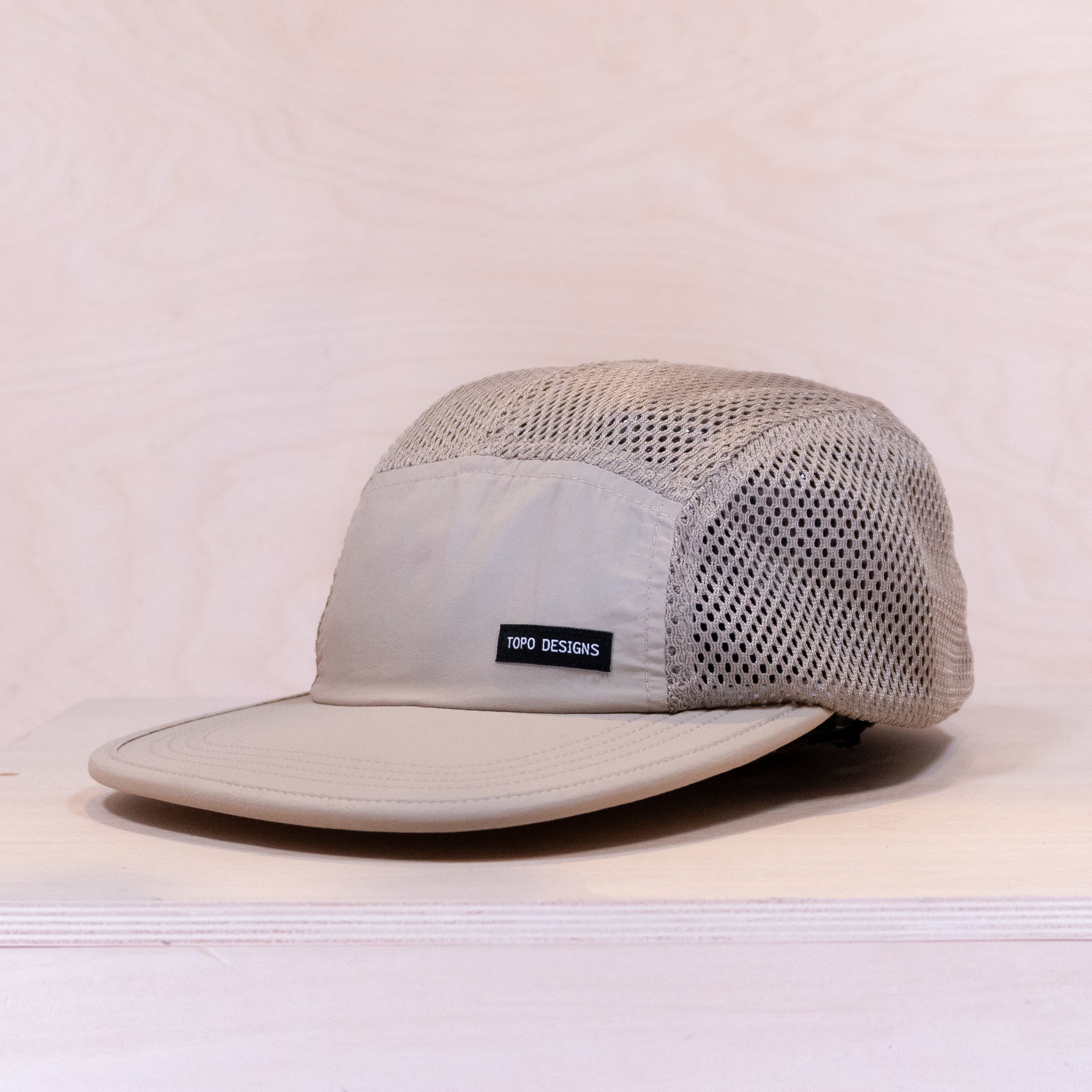 Beige cap with mesh design and Topo Designs logo on a beige background