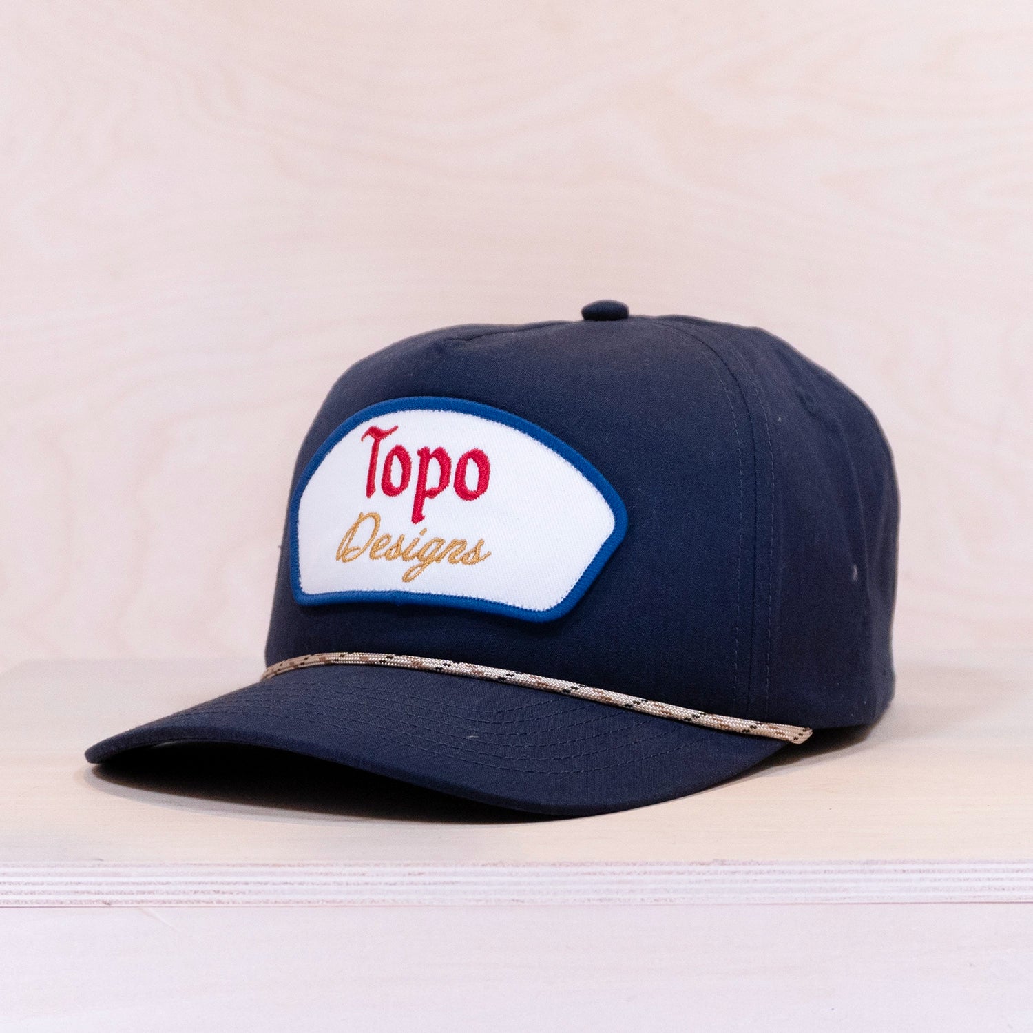 Navy blue cap with Topo Designs logo on a light beige background